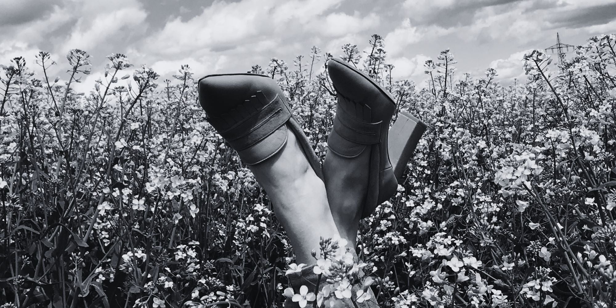 Schwarzweiß Aufnahme von Maya Nude im Rapsfeld; Schuhe gen Himmel