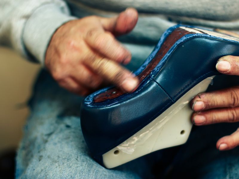 Facharbeiter traegt in Handarbeit Kleber auf Schuh auf, um Sole anzukleben.